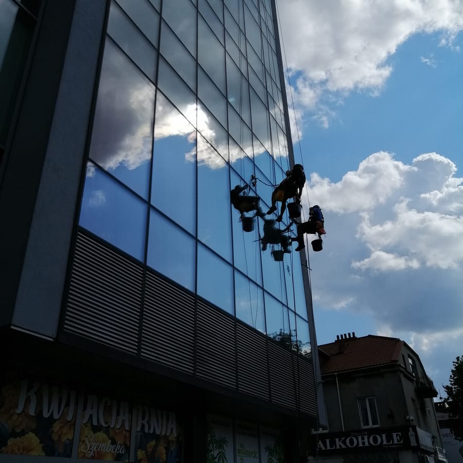 Alpiniści myjący szklaną fasadę z odbiciem chmur